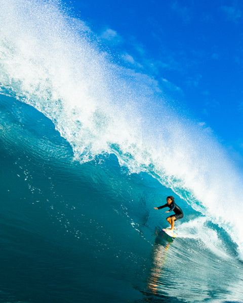 Person surfing a large wave with clear blue sky