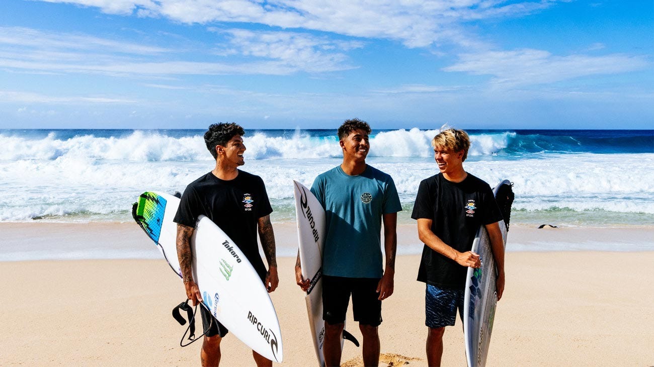 Three surfers holding surfboards on a beach with ocean waves in the background