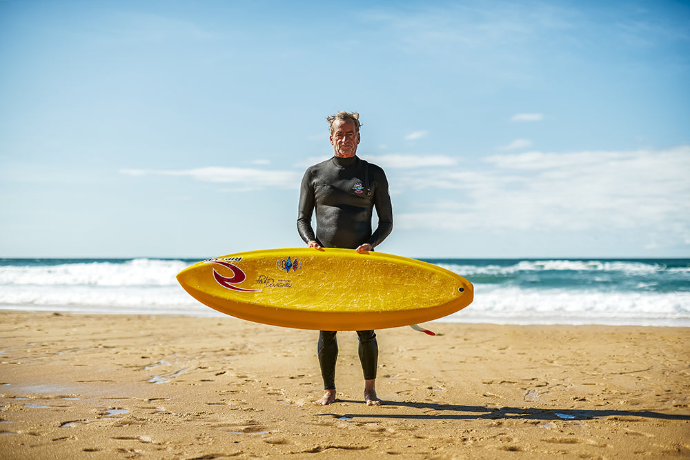 Surfer Tom Curren standing with a yellow board