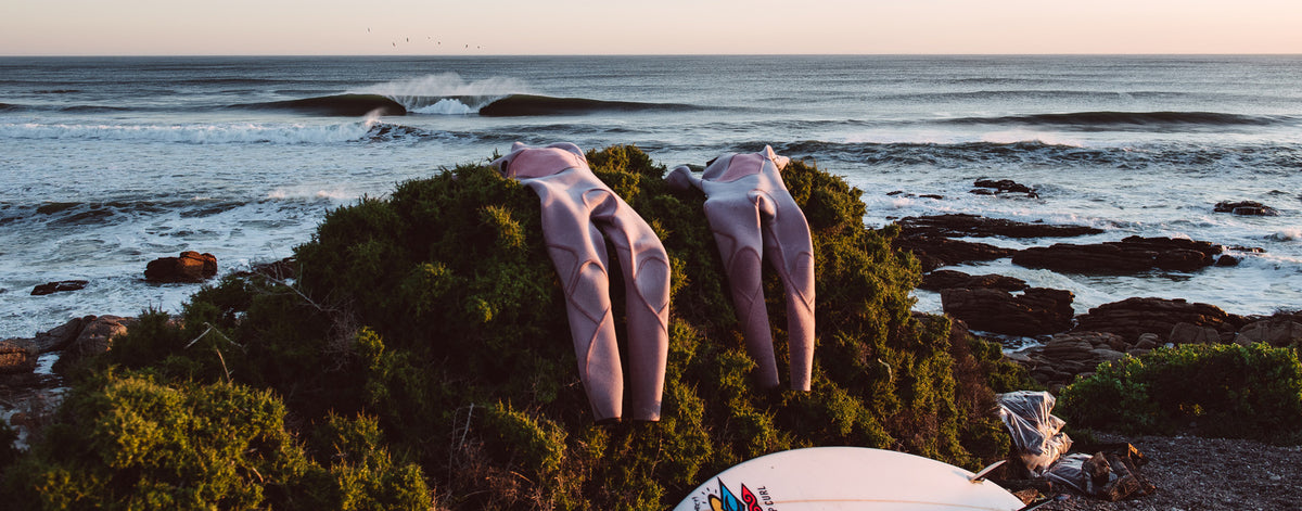 Wetsuits on a rock with a wave in the background