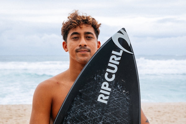 Man holding a Rip Curl surfboard on a beach
