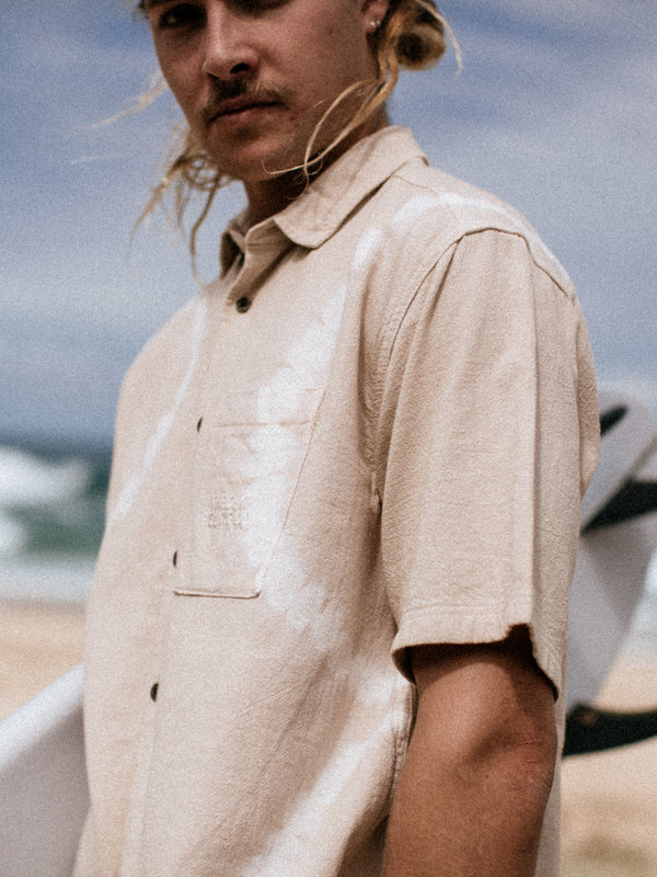 Man wearing a beige short-sleeve shirt with a blurred background