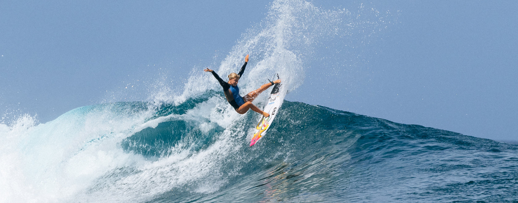 Surfer riding a wave with a clear blue sky