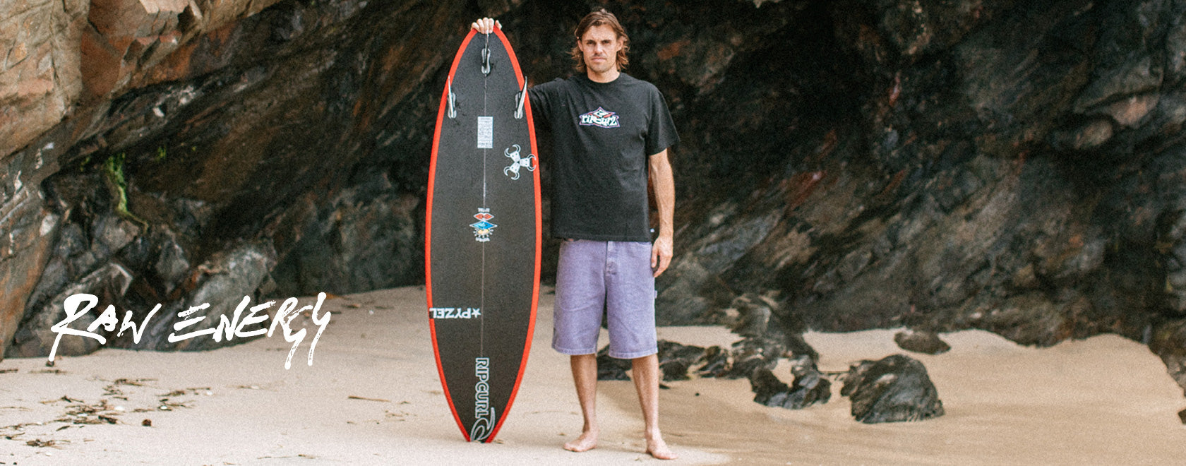 Man holding a surfboard on a beach with 'Raw Energy' branding.