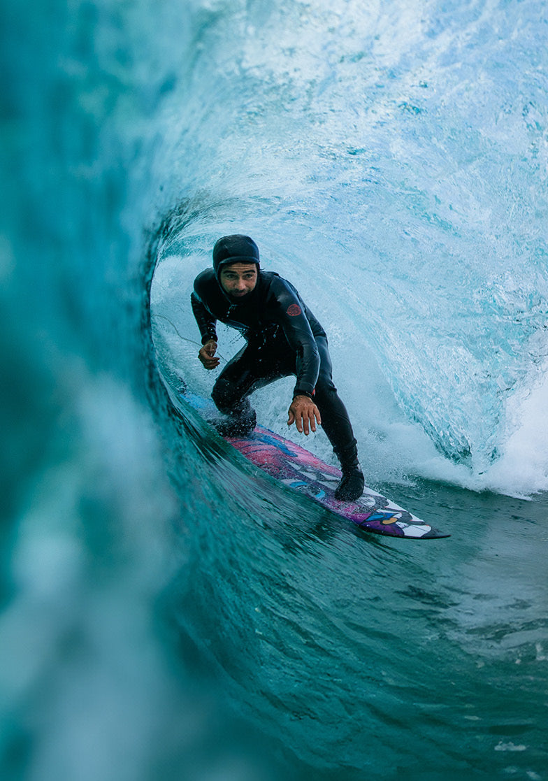 Surfer riding a wave in a black wetsuit with a colorful surfboard.