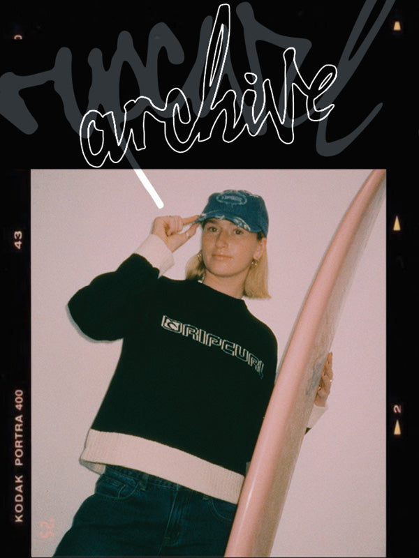 A person wearing a black and white cropped sweatshirt with 'architect' text, a blue cap, and jeans, holding a pink surfboard. The photo is styled inside a vintage film camera frame with 'architect' written across the top and 'KODAK PORTRA 400' on the left side.
