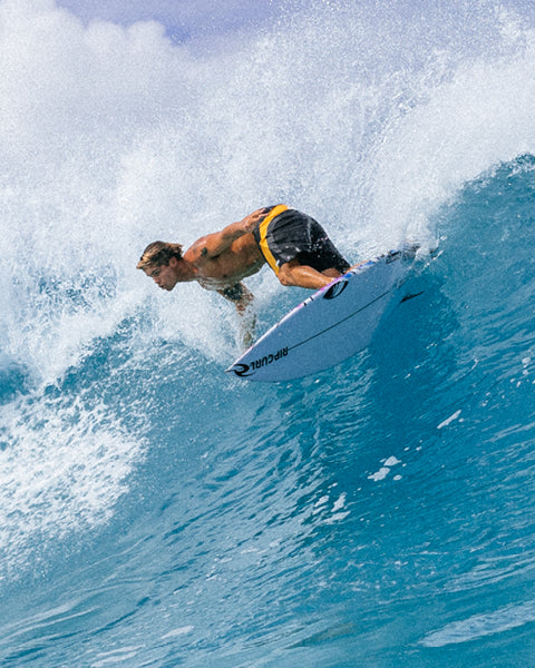 Surfer riding a wave on a surfboard with a blue sky background
