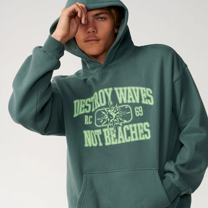 A model wearing a dark green pullover hoodie with a light green graphic print on the front that reads 'DESTROY WAVES RC NOT BEACHES' with a sunburst design.