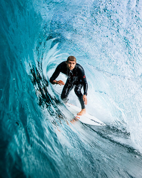 Surfer in a black wetsuit riding a blue wave.