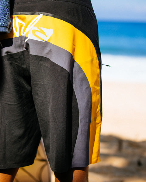 Person wearing black, yellow, and gray shorts on a beach.