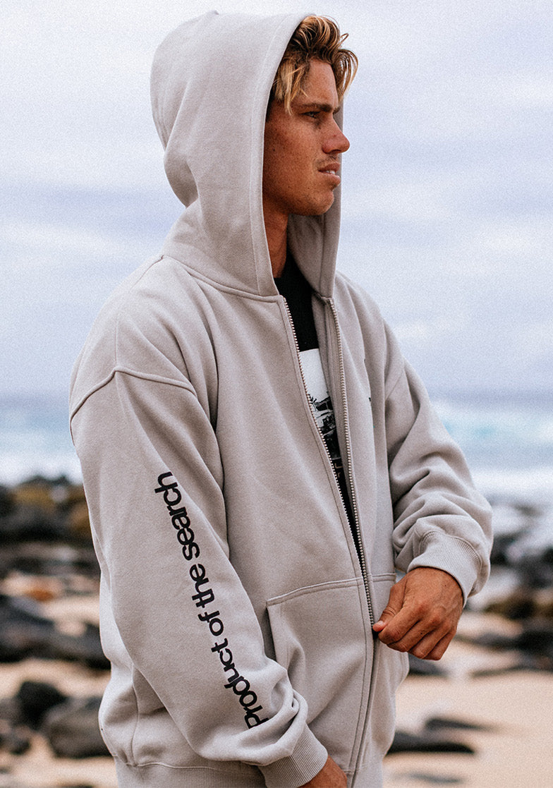 Person wearing a light gray hoodie with text on the sleeve, standing outdoors.