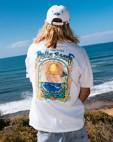Person wearing a white t-shirt with a colorful design by the ocean