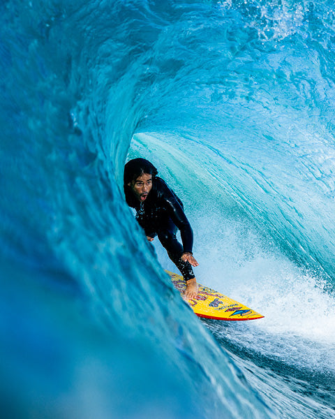 Surfer riding a wave in a black wetsuit with a yellow surfboard.