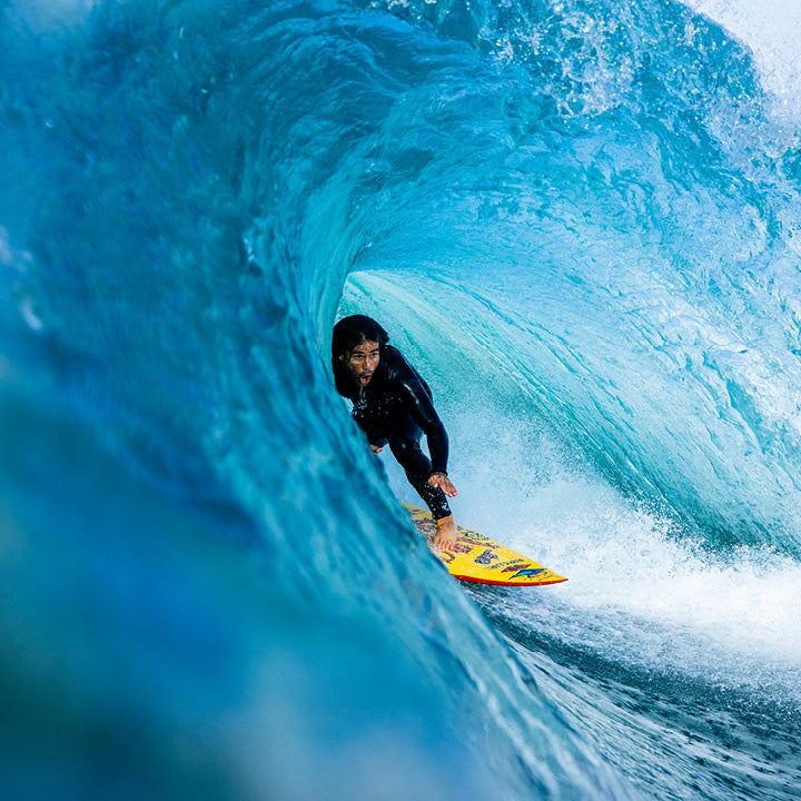 Surfer on a yellow surfboard riding a blue wave.