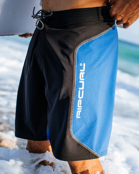 Person wearing black and blue swim shorts with 'Rip Curl' branding on a beach.