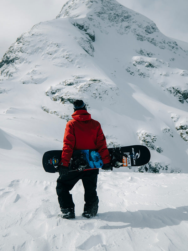 Person in a red jacket holding a snowboard on a snowy mountain