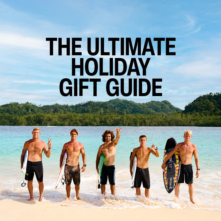 Five men on a beach with surfboards, text 'The Ultimate Holiday Gift Guide' above them.