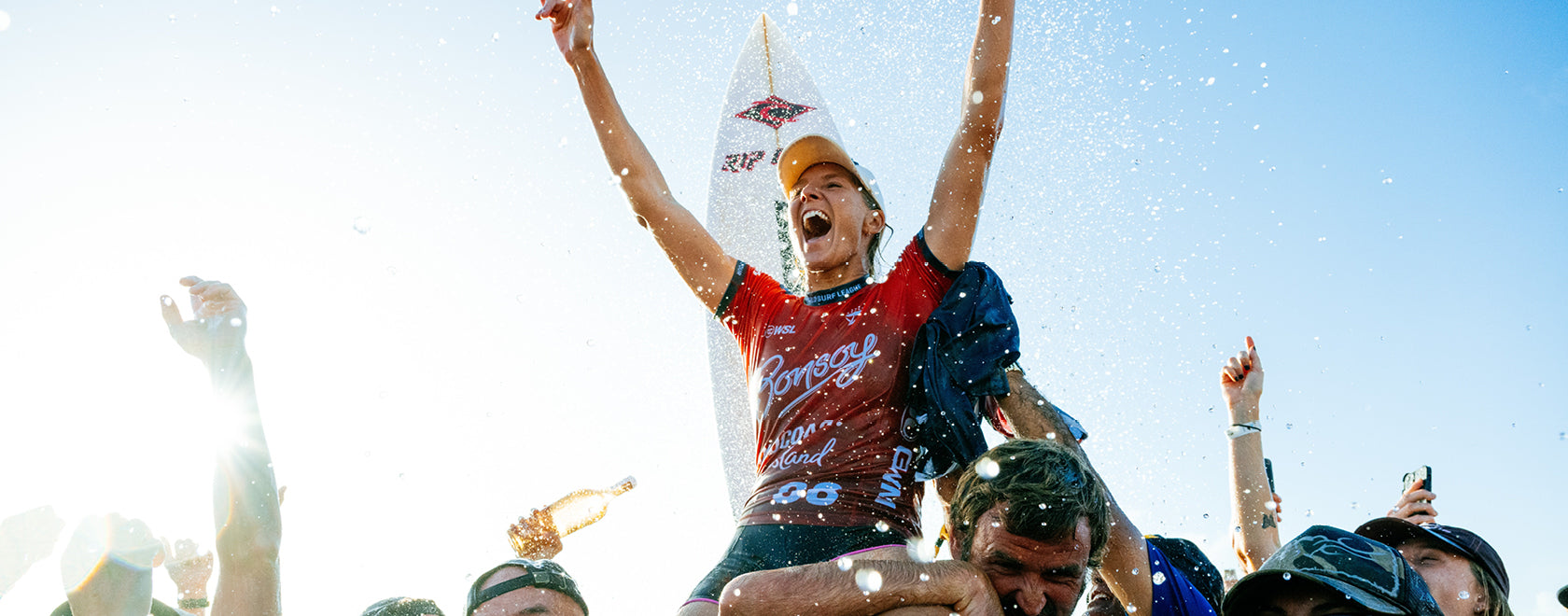 Person celebrating with arms raised, wearing a red shirt and cap, against a blue sky.
