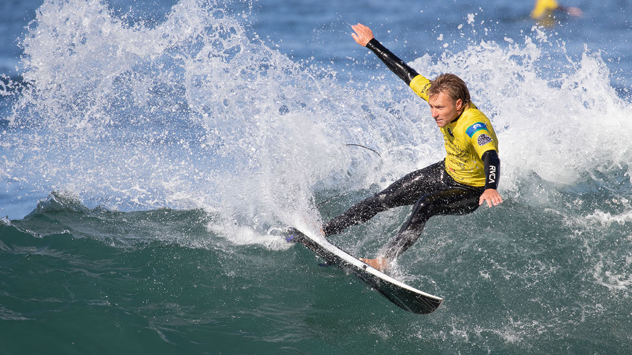 Surfer in a yellow and black wetsuit riding a wave on a surfboard.